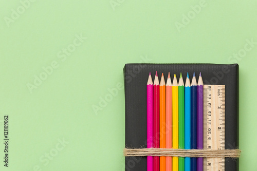 Colorful school and office supplies - pencils and ruler on black book and light green background. Top view with copy space.