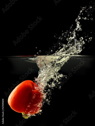 Red bell pepper falling in water with splash on black background