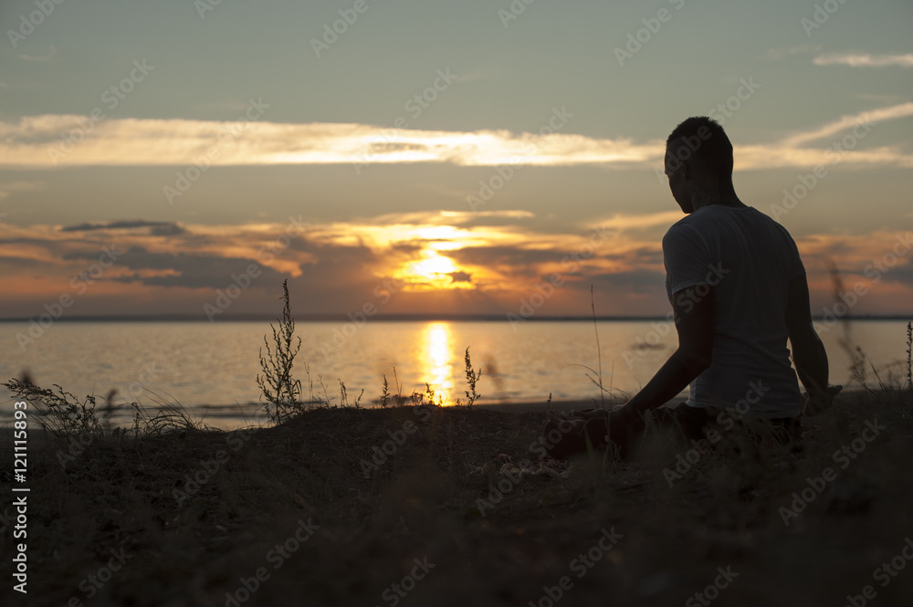Silhouette of young man practicing yoga on beach