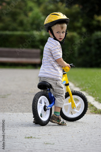 Child boy riding on his first bike with a helmet. Bike without pedals. Child learning to ride and balance on his two wheeler bike with no pedals. © Petr Bonek