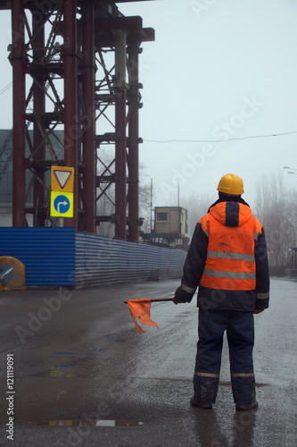 Worker in uniform with flag standing across the road preventing traffic in the construction area