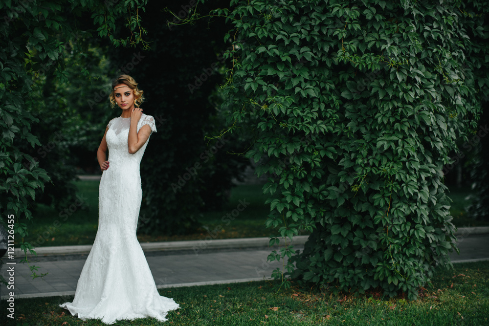 Model in a white maxi dress stands behind a pass in the park Model in a white maxi dress stands behind a pass in the park