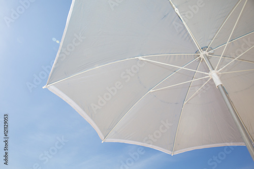 Under a grey beach umbrella looking up into the opened parasol against a blue sunny sky