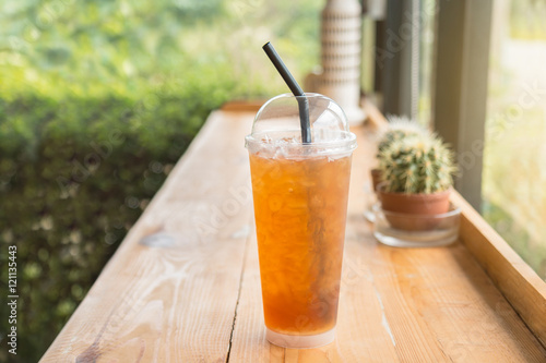 Iced lemon tea in a tall plastic cup on the wooden table. In homemade coffee shop.