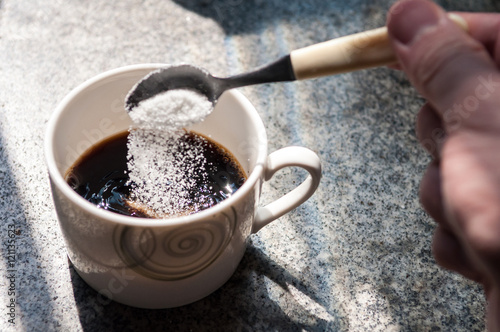 Serving sugar in coffee cup. Hand with teaspoon putting sugar in coffee cup. Sugar falling into cup of coffee.