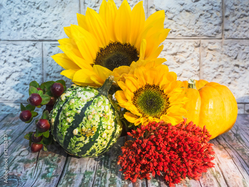 Herbstliches Arrangement mit Kürbissen und Blüten auf hölzernem Untergrund vor steinerner Mauer