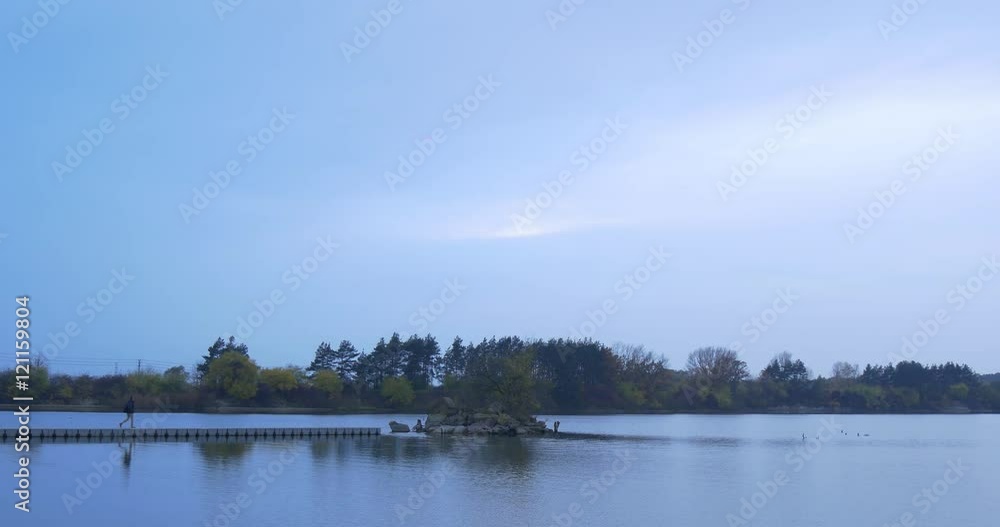 Man Comes to Wooden Pier in a Middle of a River Small Island Overgrown With Trees Autumn Landscape Yellow and Green Leaves Dusk Opposite River Bank Man Comes to Wooden Pier in a Middle of a River Small Island Overgrown With Trees Autumn Landscape Yellow and Green Leaves Dusk Opposite River Bank