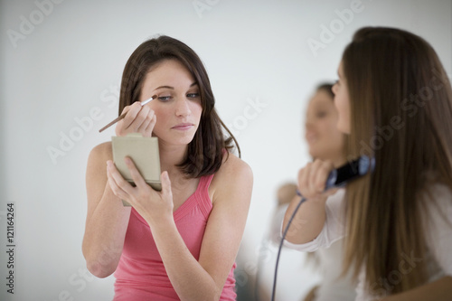 Teenage girl applying make-up while getting ready with her friend.