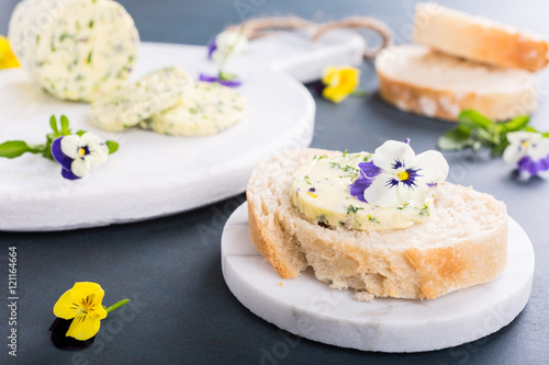 Sandwich with herb and edible flowers butter on marble cutting board. Healthy food.