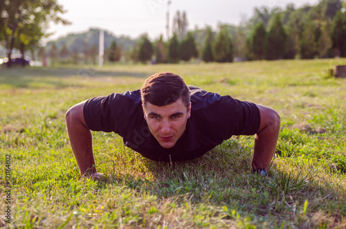 Close up of a man doing pushups on the grass with the horizon in the background.
