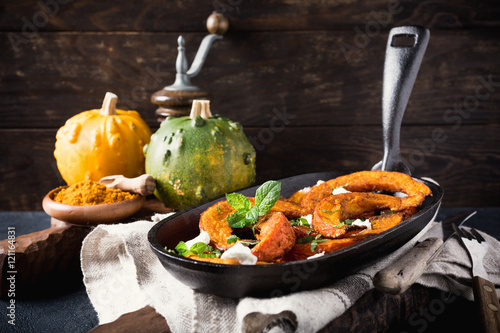 Spicy roasted pumpkin with goat cheese and mint on a cast iron skillet. Healthy food concept.