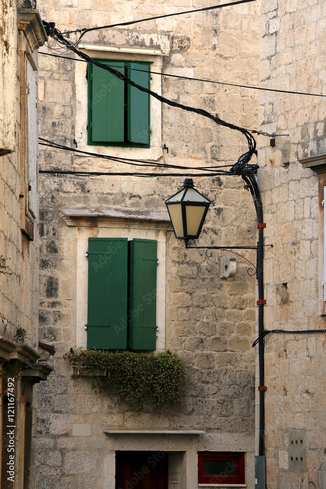Traditional mediterranean street with stone houses, picturesque windows and retro lamps. In Trogir, Croatia. Trogir is popular touristic destination and UNESCO World Heritage Site.