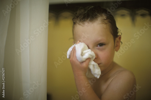 A small boy rubs his right eye with a towel. photo