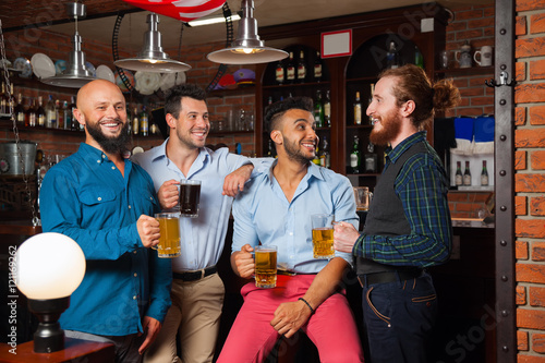 Man Group In Bar Hold Glasses Talking, Drinking Beer Mugs, Mix Race Cheerful Friends Wear Shirts