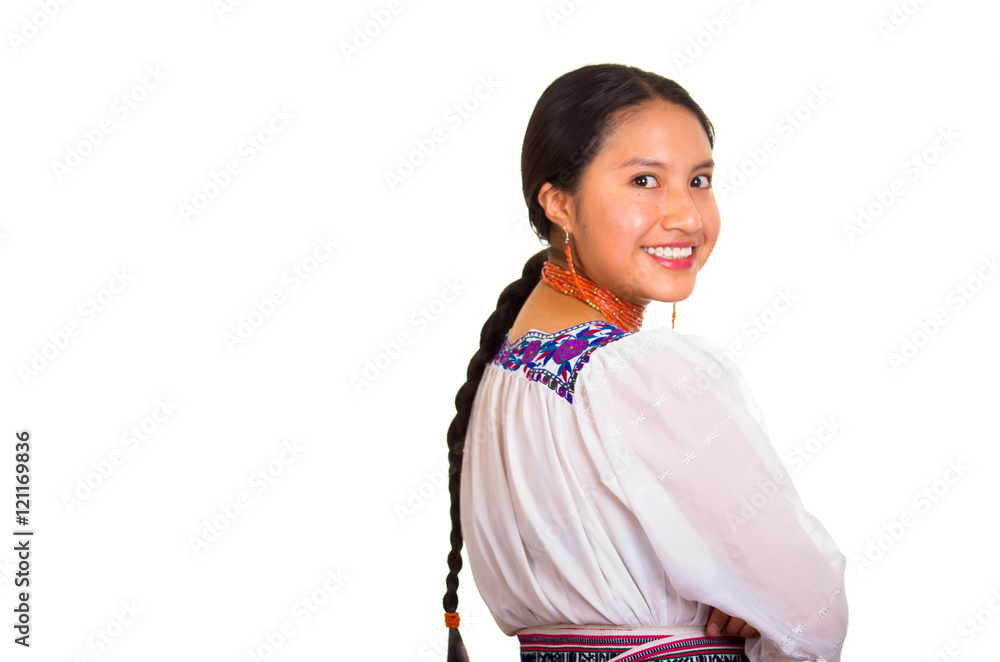 Beautiful young woman standing wearing traditional andean blouse and red necklace, turning head looking towards camera while smiling happily, white studio background Beautiful young woman standing wearing traditional andean blouse and red necklace, turning head looking towards camera while smiling happily, white studio background
