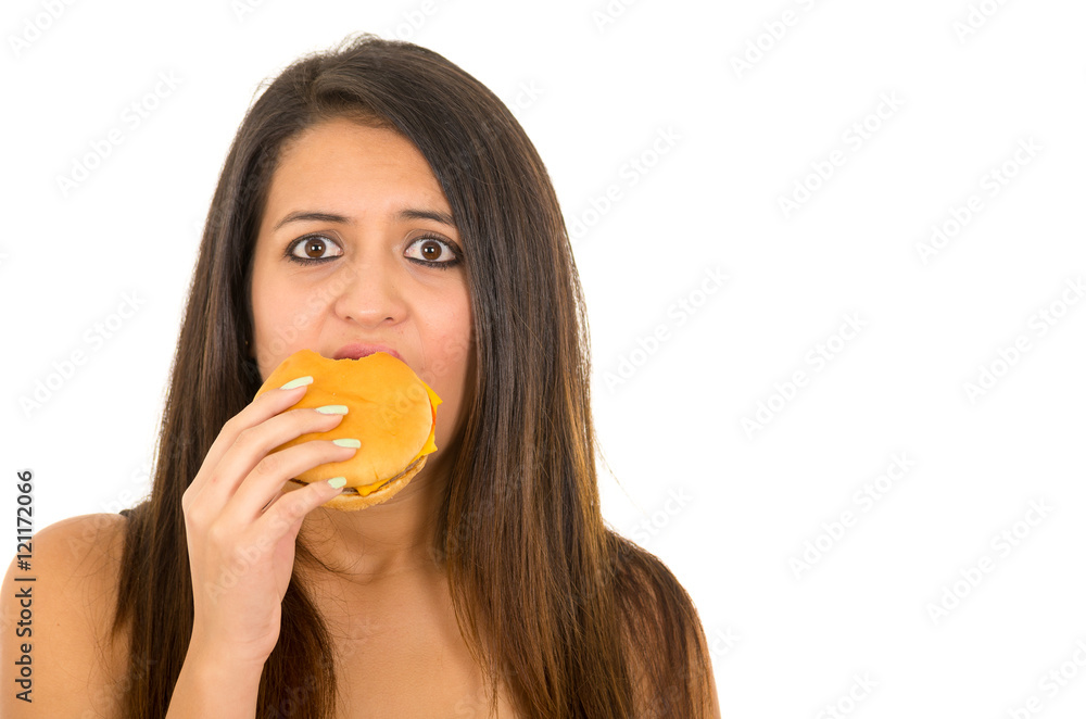 Portrait beautiful young woman posing for camera eating hamburger while making guilty facial expression, white studio background Portrait beautiful young woman posing for camera eating hamburger while making guilty facial expression, white studio background