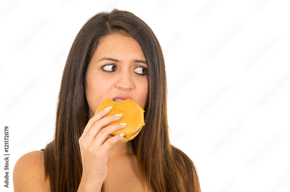 Portrait beautiful young woman posing for camera eating hamburger while making guilty facial expression, white studio background Portrait beautiful young woman posing for camera eating hamburger while making guilty facial expression, white studio background
