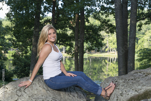 Beautiful young Caucasian woman in white tank top and denim (Blue jeans) poses in a park - model