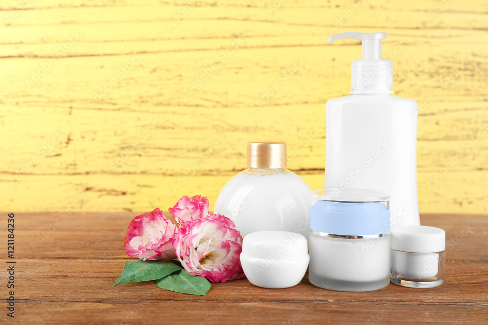 Different cosmetic bottles and eustoma flowers on yellow wall background Different cosmetic bottles and eustoma flowers on yellow wall background