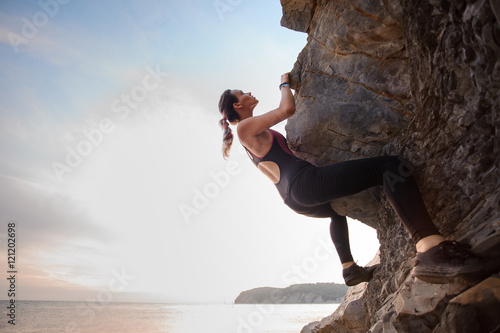 Young female rock climber climbing challenging route on overhanging cliff