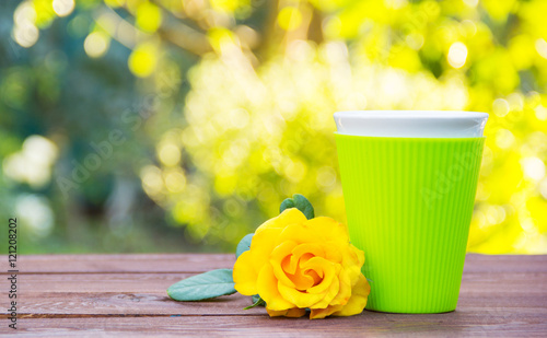 A glass of green color with a fragrant hot tea. Yellow rose and tea on a wooden table. Romantic concept. Natural green background. Green blur. Copy space.