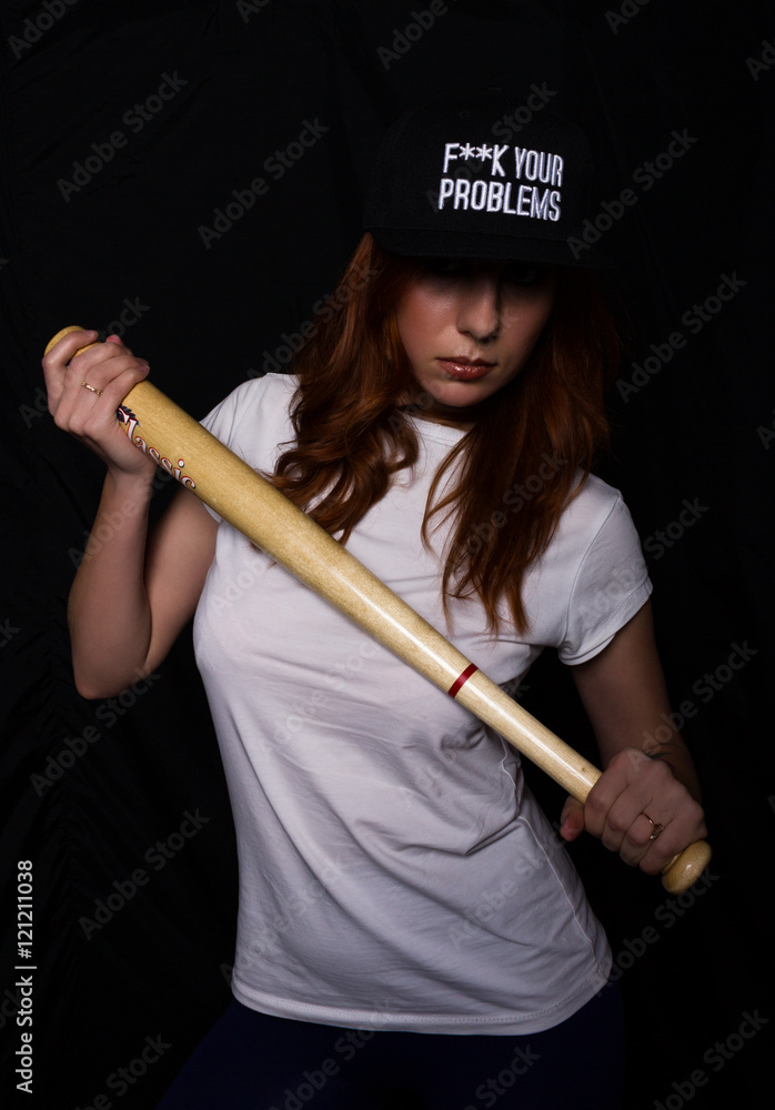 young teenager girl in a white shirt, black cap, posing with baseball bat. play of light and shadows young teenager girl in a white shirt, black cap, posing with baseball bat. play of light and shadows
