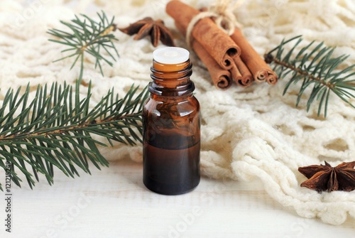Essential pine or cinnamon oil. Winter fragrances. Glass dropper bottle of aroma oil, pine twigs, cinnamon, knitted plaid. 