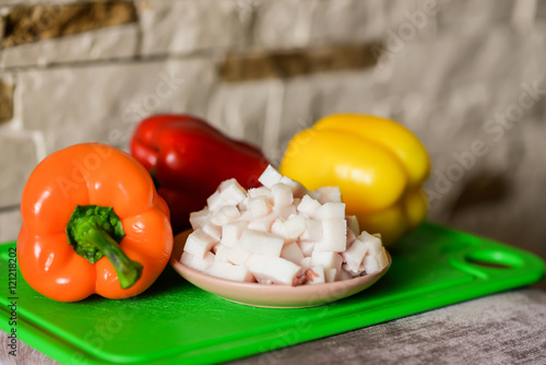 Lard cubes in small plate with colored bell peppers on green plastic board