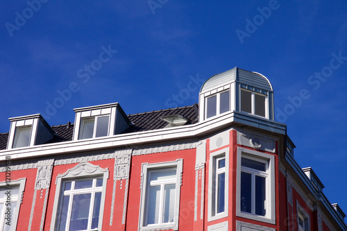 Historic Renaissance Revival architecture in the Frankenberger Quarter, Aachen, Germany with a red painted townhouse with ornate stone carving, dormer windows and hexagonal turret against a blue sky photo