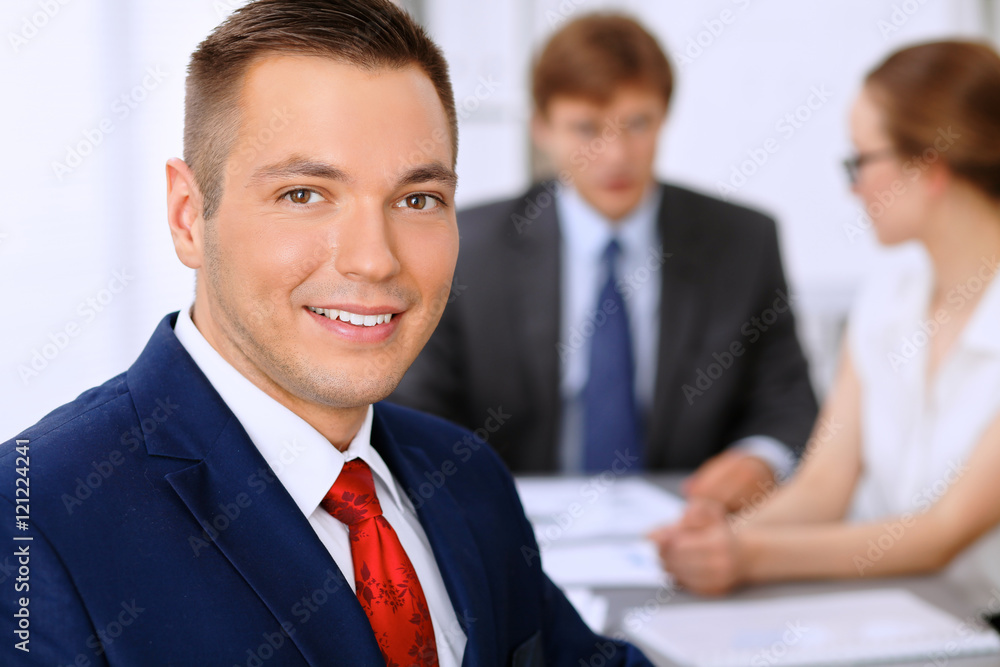 Portrait of cheerful smiling business man against a group of business people at a meeting. Portrait of cheerful smiling business man against a group of business people at a meeting.