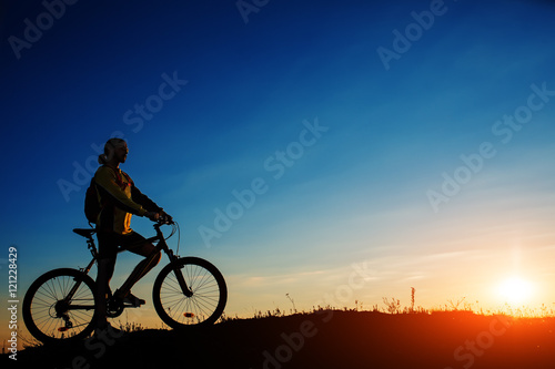 Silhouette of cyclist and a bike on sky background