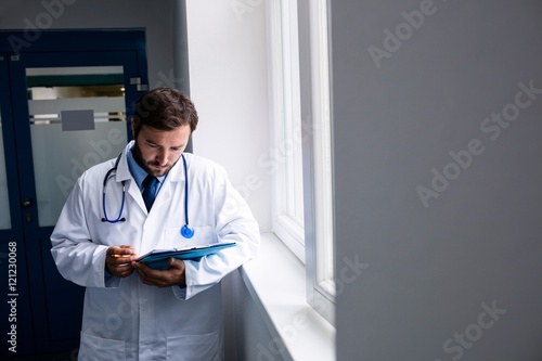 Doctor standing in corridor looking at clipboard