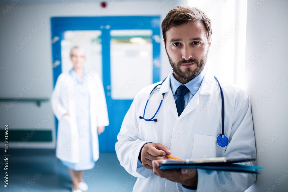 Confident doctor with clipboard standing in hospital corridor Confident doctor with clipboard standing in hospital corridor