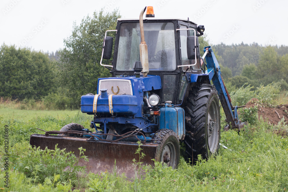 Old blue tractor-excavator stands in a meadow in the rain Old blue tractor-excavator stands in a meadow in the rain