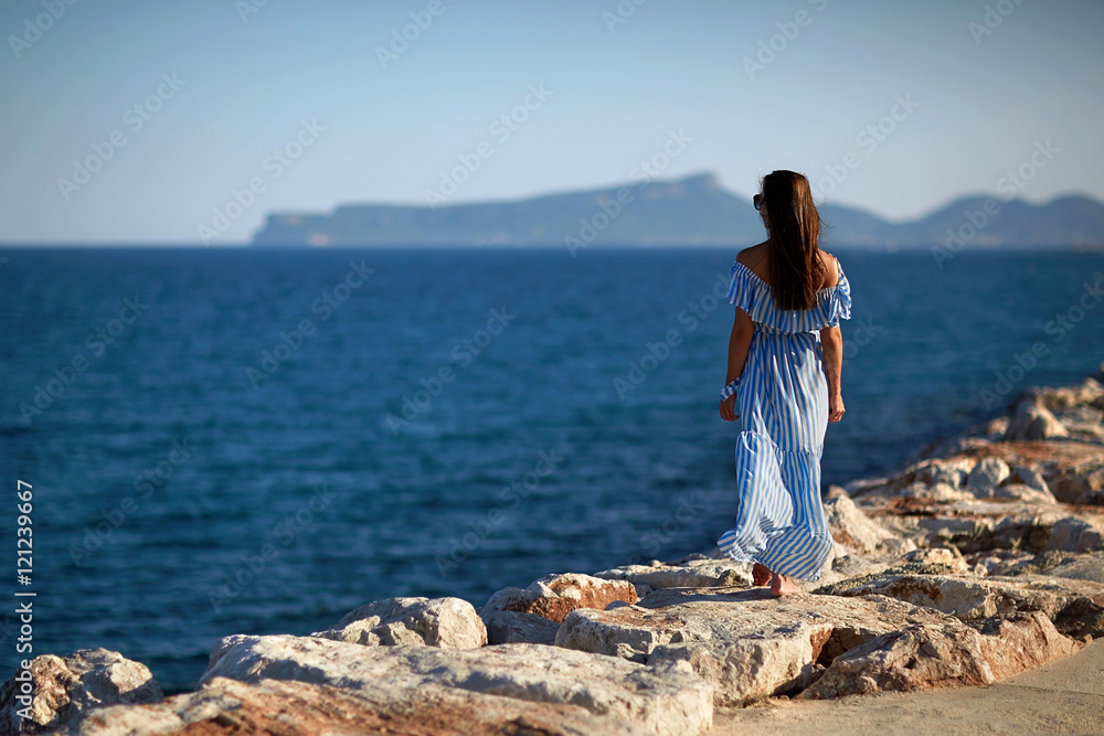 Woman walking along the sea on the rocks in the blue dress and l