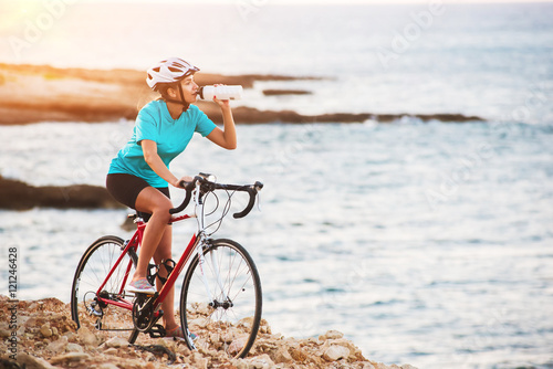 Female cyclist standing on a rock with bike and drinking water