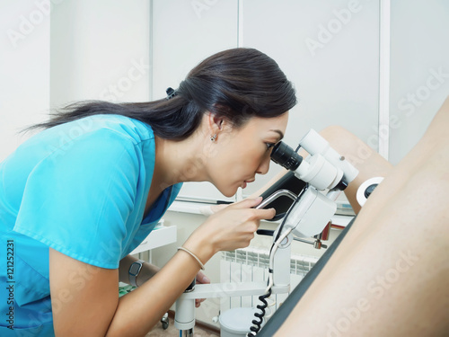 Asian gynecologist examining patient in hospital using a colposcope photo