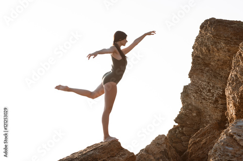 Beautiful ballerina dancing, posing on rock at beach, sea background.