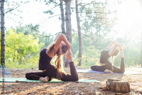 two women practicing yoga in the wood. Group of people practicing yoga during sunset or sunrise