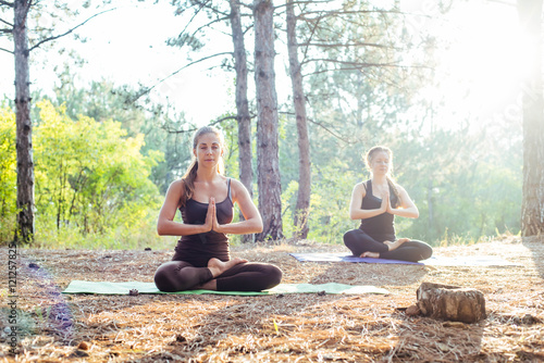 two women practicing yoga in the wood. Group of people practicing yoga during sunset or sunrise