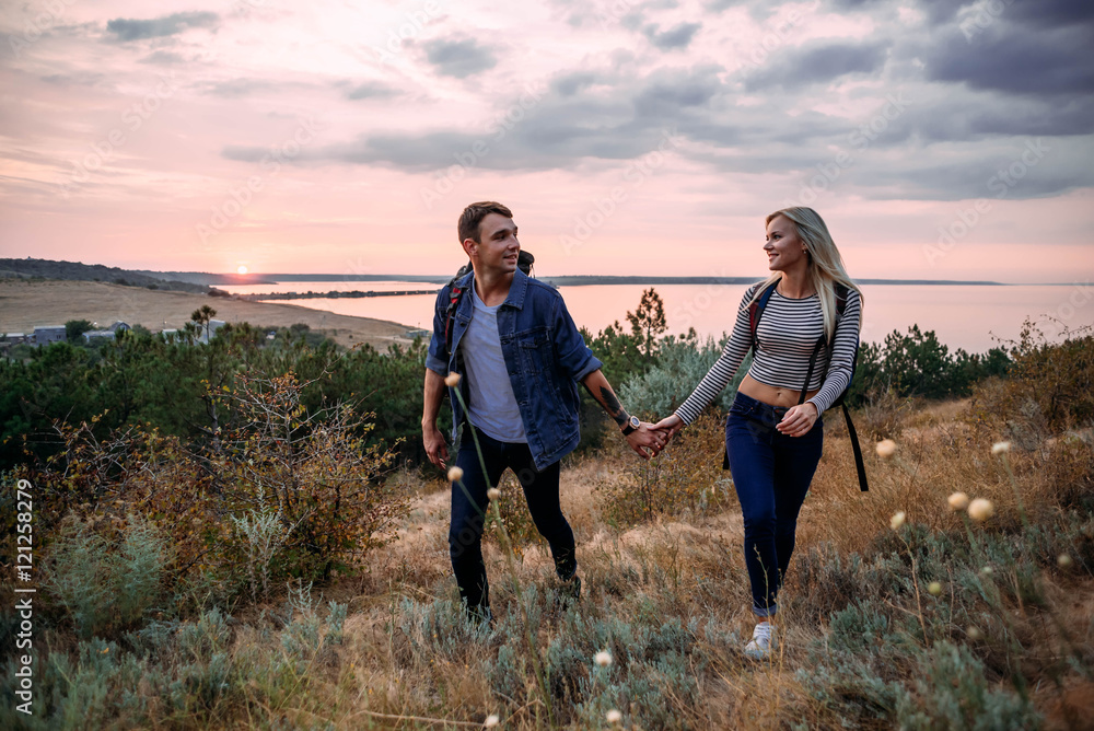 Young caucasian couple hiking outdoors with backpacks during sunset