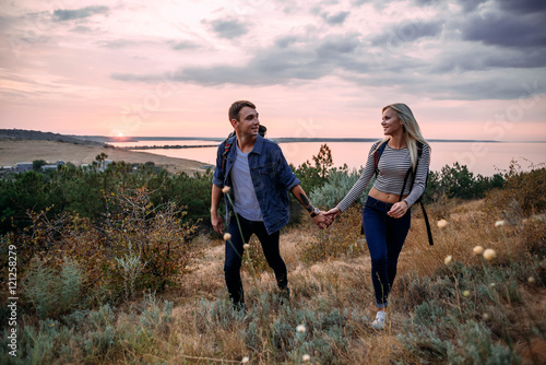 Young caucasian couple hiking outdoors with backpacks during sunset