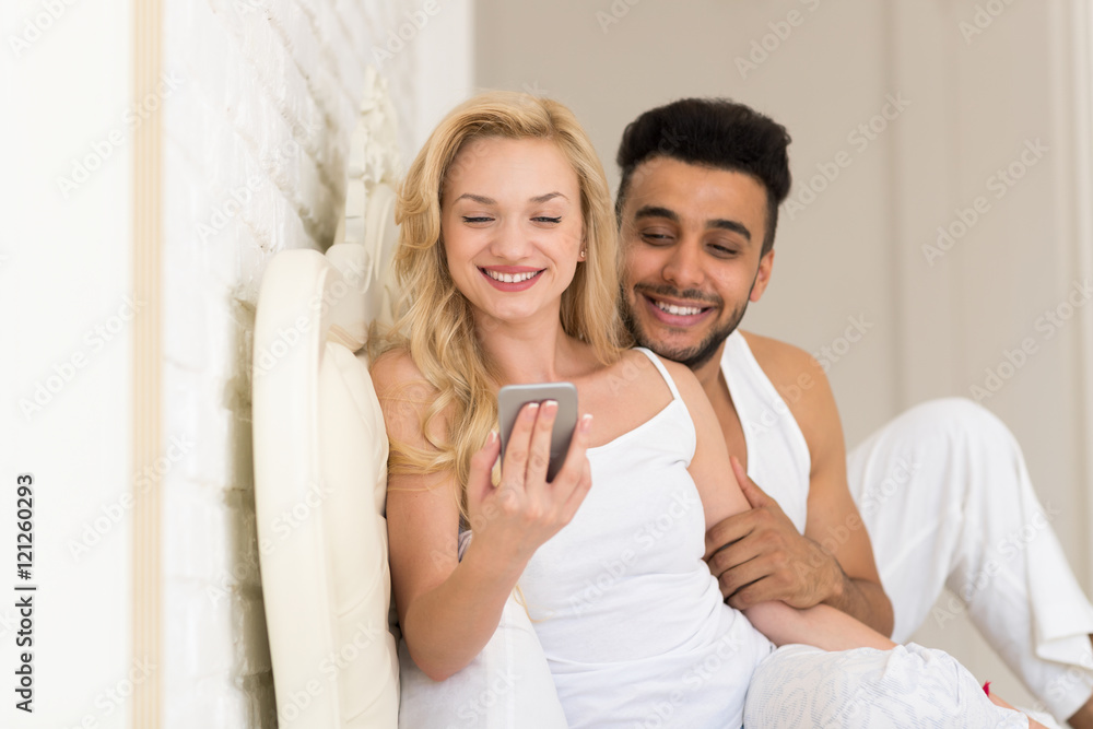 Young Couple Lying In Bed, Happy Smile Hispanic Man And Woman Using Cell Smart Phone Young Couple Lying In Bed, Happy Smile Hispanic Man And Woman Using Cell Smart Phone