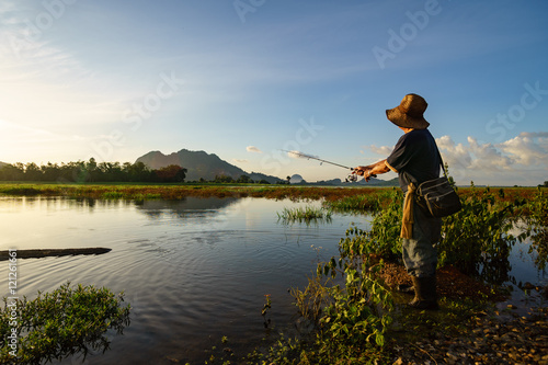 An angler wearing old hat was fishing by the lakeside alone.
