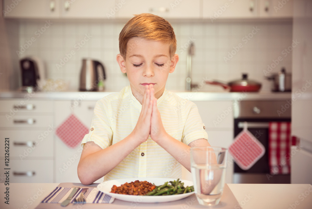 Cute little boy saying prayer before eating meal