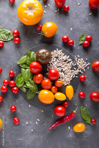 Tomatoes of different varieties  basil  sunflower seeds on a slate on a gray background