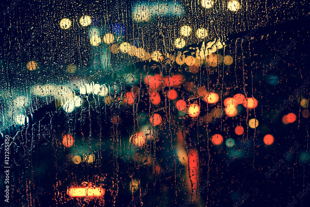 City view through a window on a rainy night,Rain drops on window with road light bokeh, City life in night in rainy season abstract background. - obrazy, fototapety, plakaty 