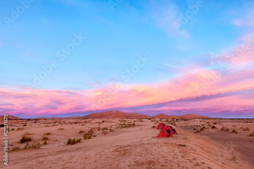 Sahara Desert camp at sunrise with a row of red tents in the sand. Adventure travel.