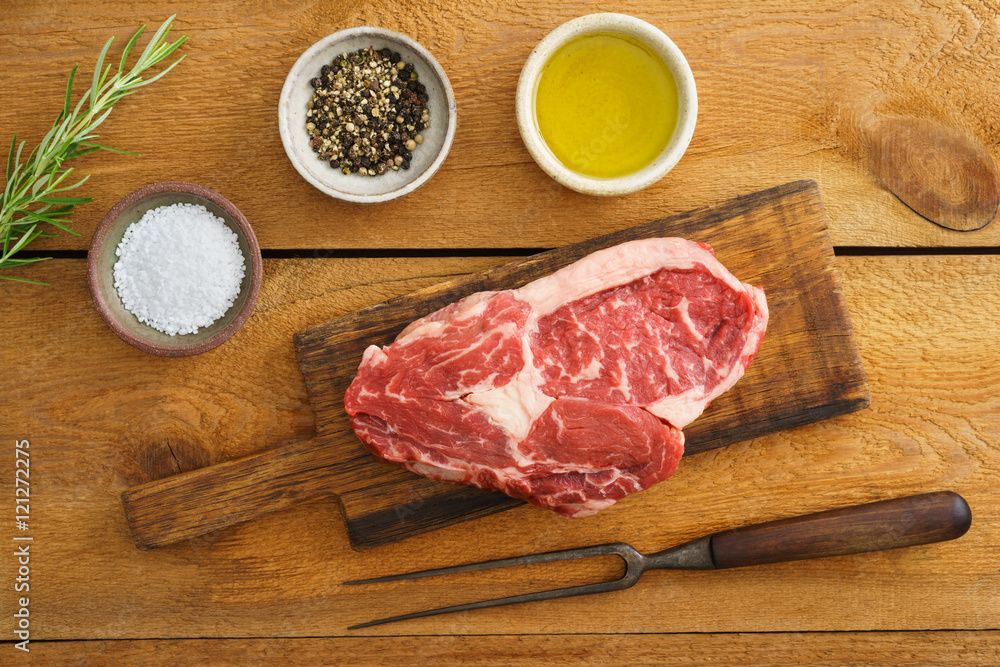 Uncooked rib eye steak on wooden board on wood Uncooked rib eye steak on wooden board on wood