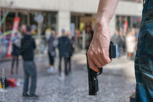 Armed man (attacker) holds pistol in public place. Many people on street. Gun control concept.